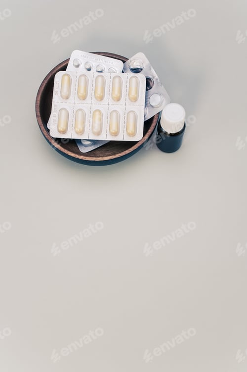 Preview: Small bowl full of pill blister packs and a vial isolated on a beige background