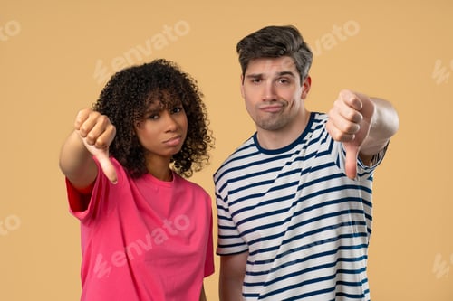 Preview: Interracial Couple Giving Thumbs Down Dislike With Disapproving Look On Beige