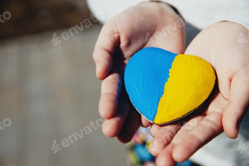 Preview: Small little kid hold heart shaped stone with Ukraine national flag or anthem