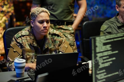Preview: Young multiethnic female military officer in camouflage uniform using laptop