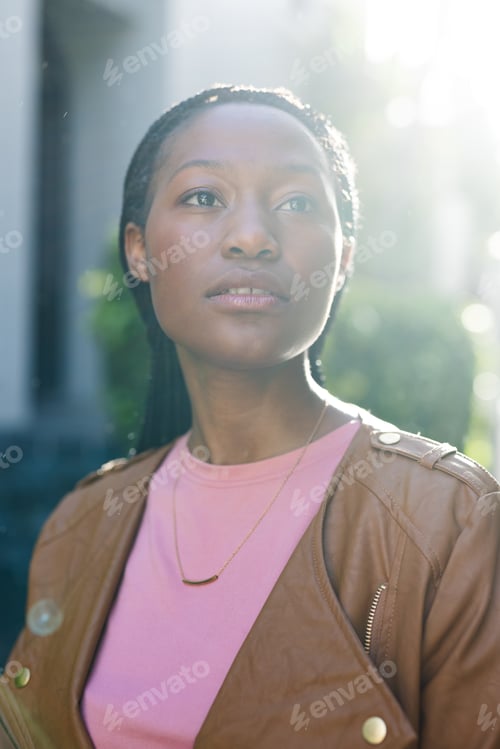 Preview: African american woman wearing leather jacket looking away, standing outside house