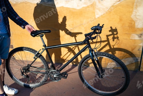 Preview: Man with smart phone and bicycle standing in front of brick wall
