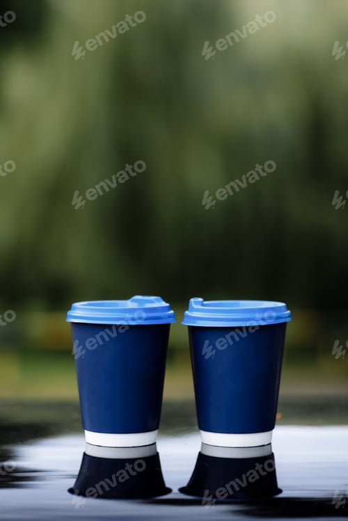 Preview: two blue paper coffee Cup with on car roof. Paper Cup with hot tea on the black mirror on nature