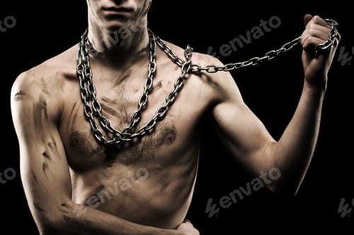 Preview: Young athletic man in massive chains on arms over black background