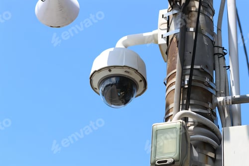 Preview: Surveillance camera mounted on a utility pole against a clear blue sky