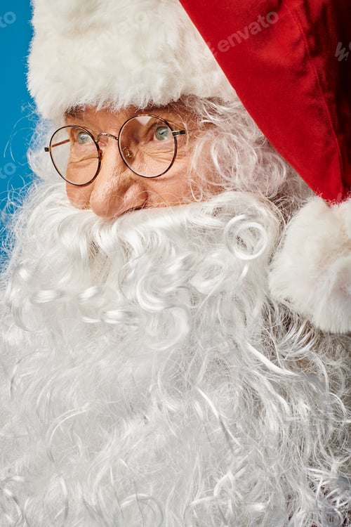 Preview: close up of happy Santa Claus with white beard and eyeglasses looking away on blue background