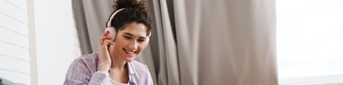Preview: The smiling curly woman listening to music on headphones while sitting in the room