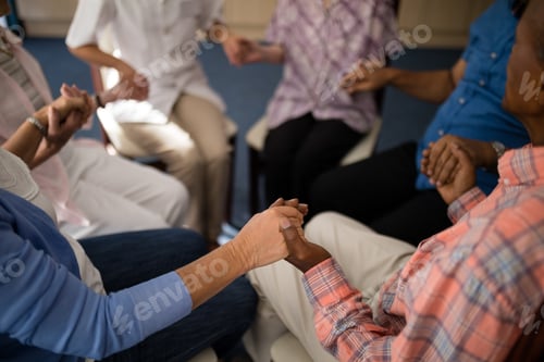 Preview: High angle view of seniors and female doctor holding hands while sitting on chairs