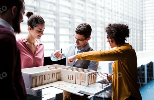 Preview: Group of young architects with model of a house standing in office, talking.