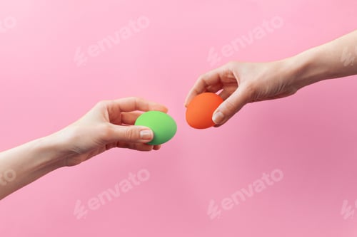 Preview: Woman hands holding Easter eggs for knocking on pink background. Easter celebration or creative