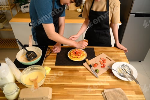 Preview: Loving young couple decorating homemade pancakes with sliced strawberries together