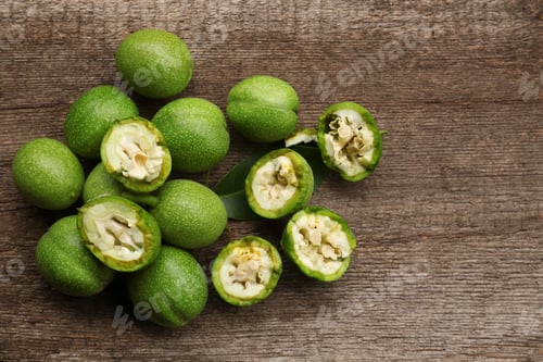 Preview: Whole and broken green walnuts on wooden table, flat lay