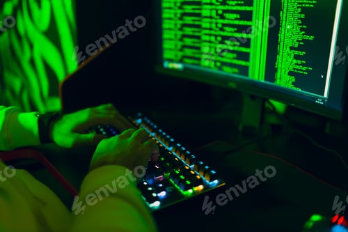 Preview: Hacker in hoodie working hacks code site on personal computer with green light