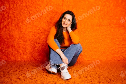 Preview: Young woman sitting on orange shag carpet with matching orange sweater and blue jeans