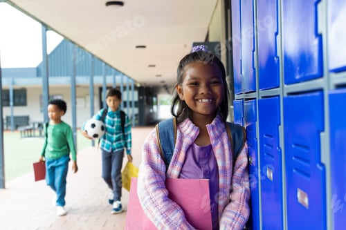 Preview: Biracial girl with a purple backpack smiles by school blue lockers, boys in the background