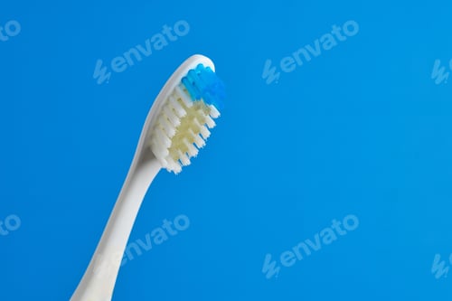 Preview: Shiny toothbrush with blue and white bristles on plain blue background