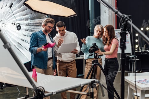 Preview: selective focus of art director holding pink shoe near coworkers in photo studio