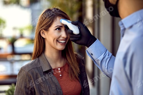 Preview: Happy woman getting her temperature measured with infrared thermometer.