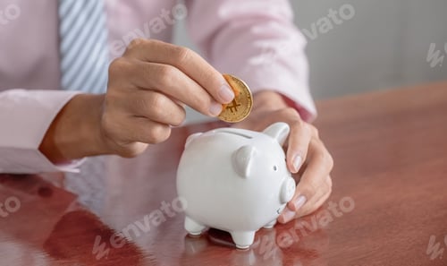 Preview: Businessman hand putting bitcoin into white piggy bank