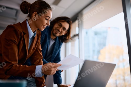 Preview: Happy entrepreneur analyzing business reports with her coworker in the office.