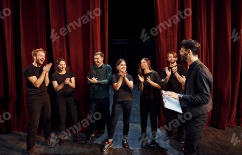 Preview: Man is practicing his role. Group of actors in dark colored clothes on rehearsal in the theater