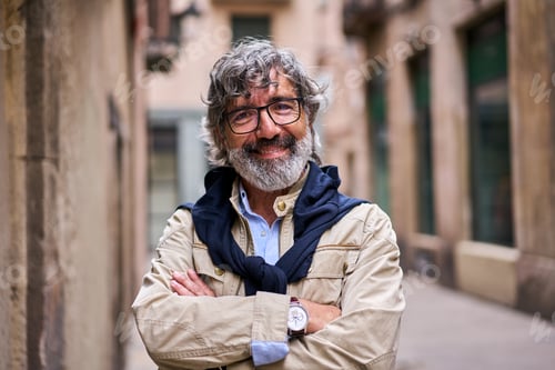 Preview: Senior gray haired man crossed arms smiling happy looking at camera standing on city street.