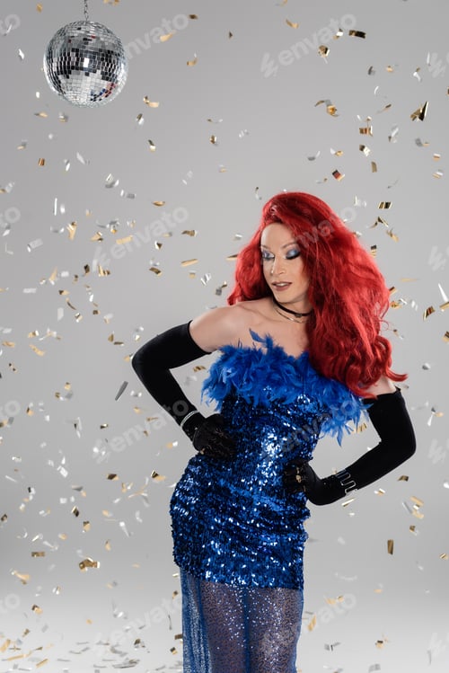 Preview: Smiling drag queen in elegant dress and gloves posing under confetti and disco ball on grey