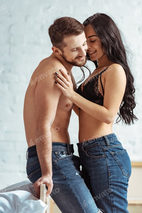 Preview: handsome and muscular man hugging with beautiful and smiling woman in lace bra in bedroom