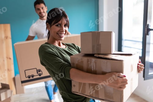 Preview: Beautiful young couple holding cardboard boxes while moving to new home. Looking at camera.