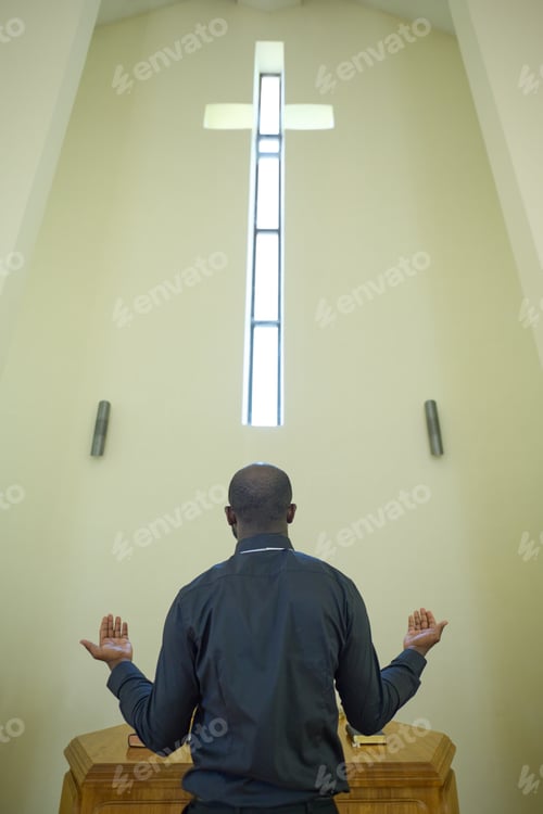 Preview: Rear view of young African American pastor in black apparel praying in church