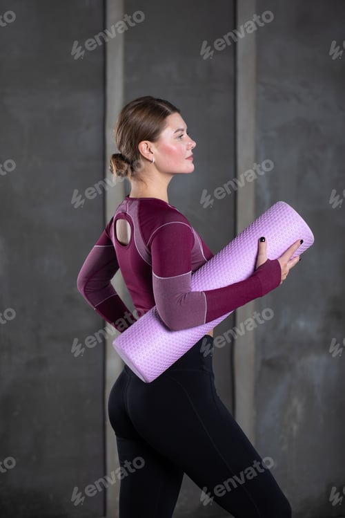 Preview: A sporty attractive woman stands with a roller for self-massage. Myofascial release.