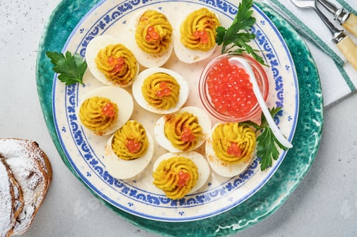 Preview: Stuffed eggs with red caviar and paprika on plate for appetizer easter table, top view, copy space.