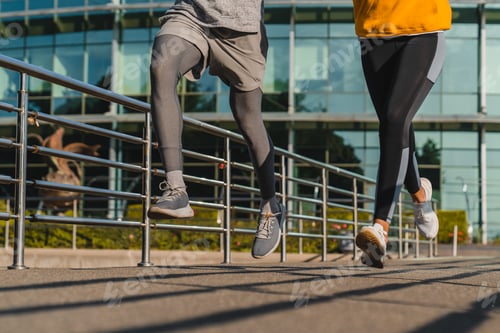 Preview: Cropped photo of young jogger`s legs while running against urban background