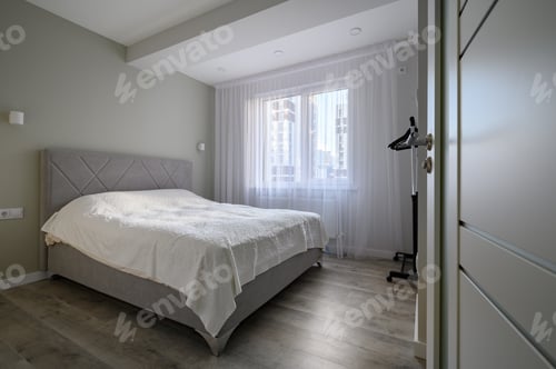 Preview: Open door to bright white bedroom with double bed