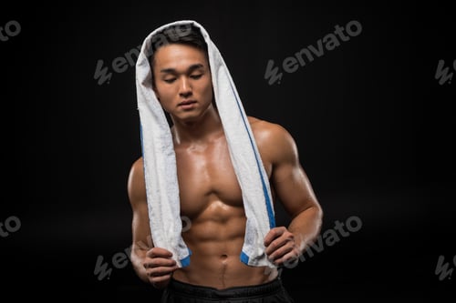 Preview: shirtless muscular asian man with towel on head looking down isolated on black