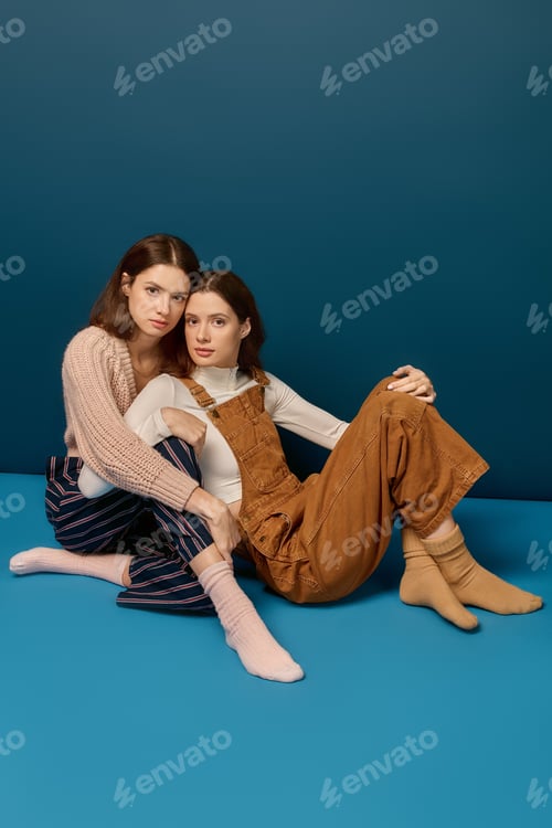 Preview: Young beautiful twin sisters posing together in a cozy setting, radiating harmony and joy