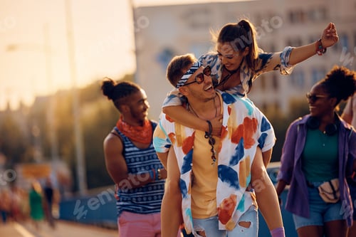 Preview: Cheerful man piggybacking his girlfriend while going to summer music festival.