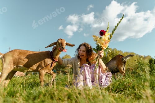 Preview: Smiling woman enjoying nature with goats and flowers on a sunny day