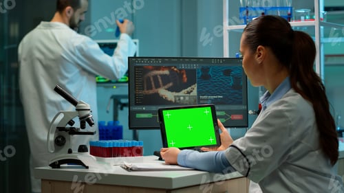 Preview: Biochemist sitting in laboratory using green mock-up screen tablet