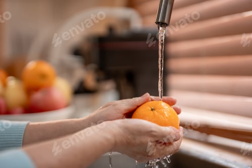 Preview: Close up hand of senior woman housewife wash orange in kitchen at home.