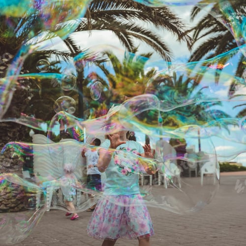 Preview: Pretty little girl is playing with big bubbles in street in summer day