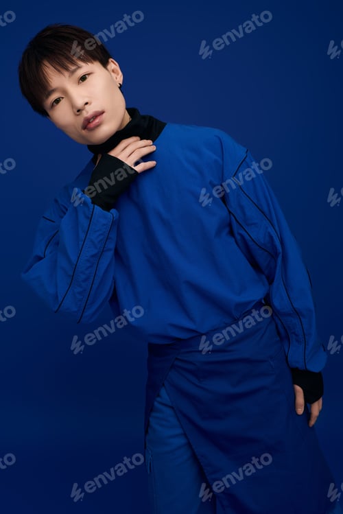 Preview: Captivating young asian man in bold blue outfit striking a stylish pose against a vibrant backdrop