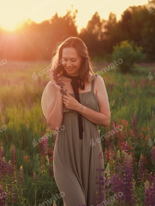 Preview: beautiful girl with a purple flowers walks at sunset in a flower field in the countryside