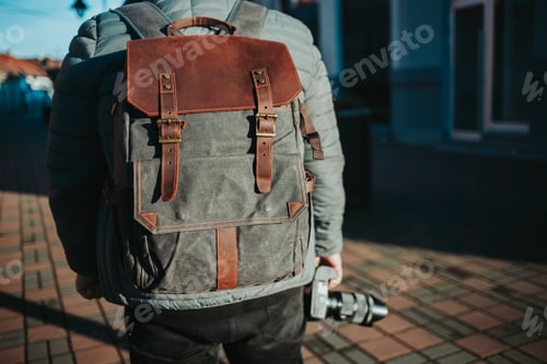Preview: Shallow focus shot of a male wearing a grey and brown rucksack and holding a camera