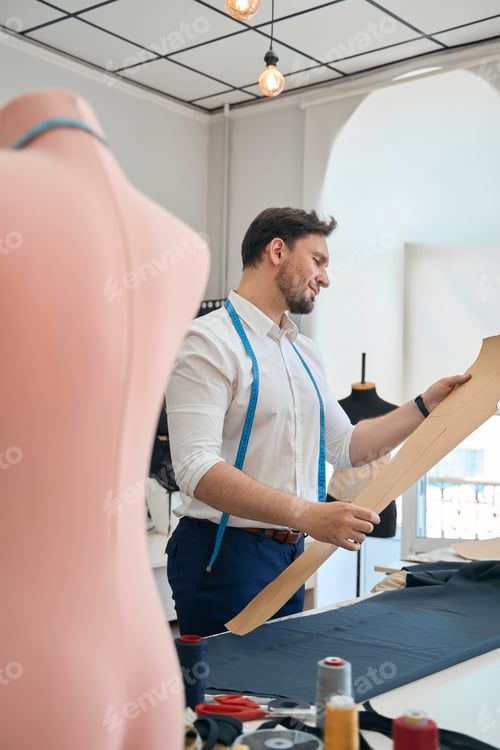 Preview: Man couturier works with pattern in a sewing workshop
