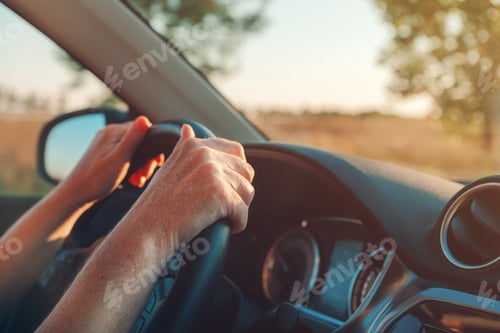 Preview: Female hands on the vehicle steering wheel, inside the car, driving through countryside