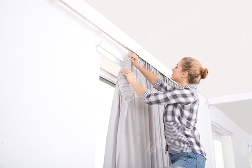 Preview: Woman hanging window curtain indoors. Interior decor element