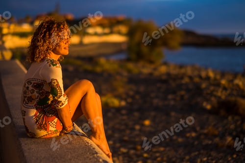 Preview: One woman sit down outdoor and enjoy sunset light looking in front of her - beach and ocean