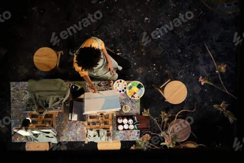 Preview: From above view of skilled female student painting picture on canvas in dark creative studio.