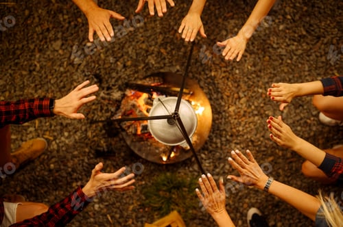 Preview: Friends warming their hands by campfire, camping